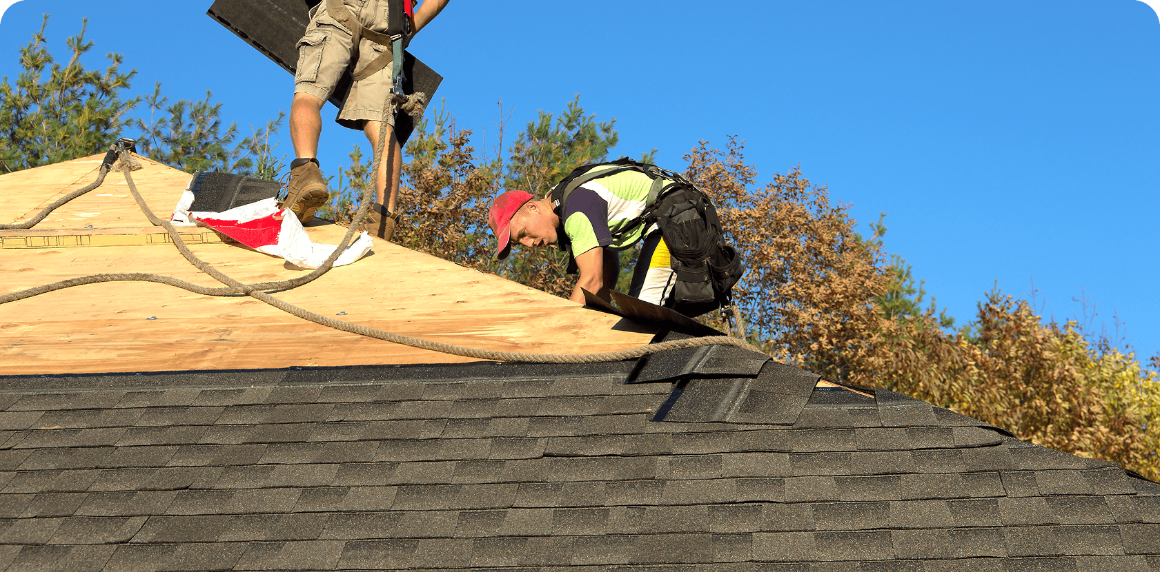 Workers installing roof shingles on house.