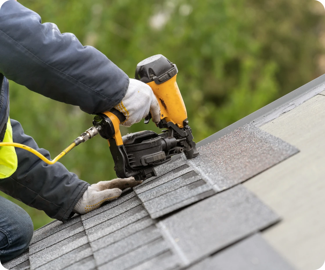 Roofer using nail gun on shingles.